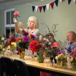 A woman holds up a prize winning rose in a small vase